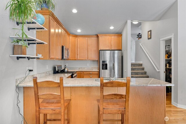 kitchen featuring light stone counters, stainless steel appliances, a kitchen breakfast bar, and kitchen peninsula