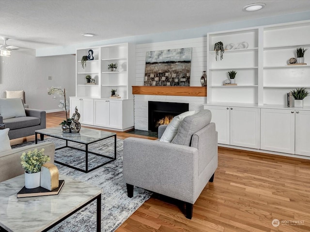 living room with a fireplace, ceiling fan, a textured ceiling, light wood-type flooring, and built in shelves