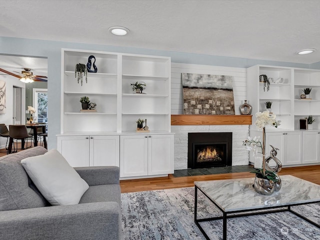 living room featuring ceiling fan, built in shelves, light hardwood / wood-style flooring, and a textured ceiling