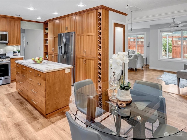 kitchen featuring crown molding, light hardwood / wood-style flooring, appliances with stainless steel finishes, hanging light fixtures, and a center island