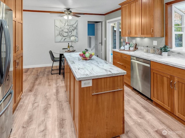 kitchen with stainless steel appliances, a center island, light stone countertops, ornamental molding, and light wood-type flooring