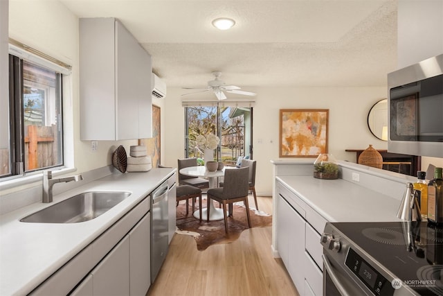 kitchen with sink, a wall mounted air conditioner, a textured ceiling, light wood-type flooring, and appliances with stainless steel finishes