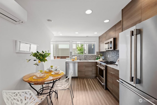 kitchen featuring sink, high end appliances, tasteful backsplash, light hardwood / wood-style floors, and an AC wall unit