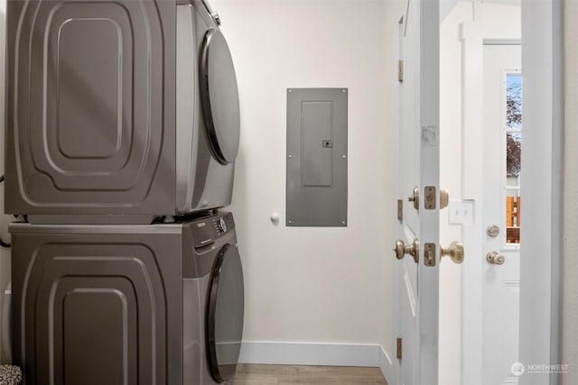 laundry area with electric panel, stacked washer and clothes dryer, and light wood-type flooring