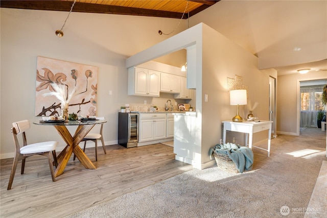 kitchen with lofted ceiling with beams, sink, wine cooler, white cabinets, and light hardwood / wood-style floors