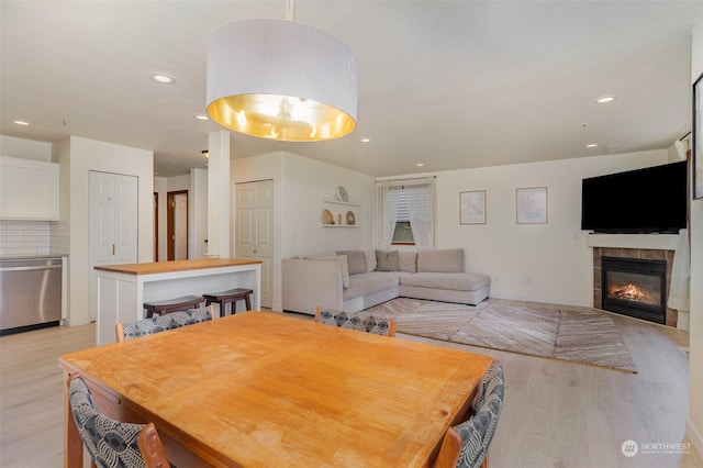 dining room with a tiled fireplace and light hardwood / wood-style flooring