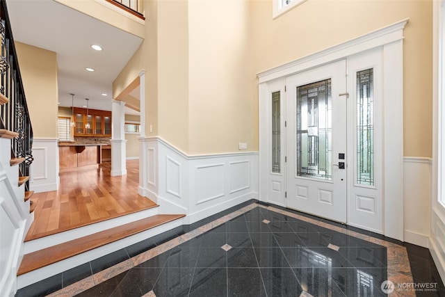 foyer entrance with wainscoting, a decorative wall, granite finish floor, and recessed lighting