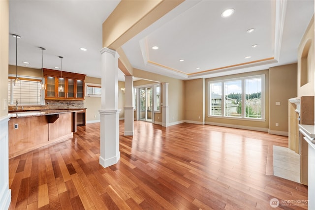 unfurnished living room with a tray ceiling, light wood-style flooring, and decorative columns