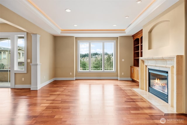 unfurnished living room with ornamental molding, light wood finished floors, a fireplace, and a raised ceiling