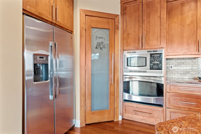 kitchen with backsplash, light stone counters, stainless steel appliances, and dark wood-style flooring