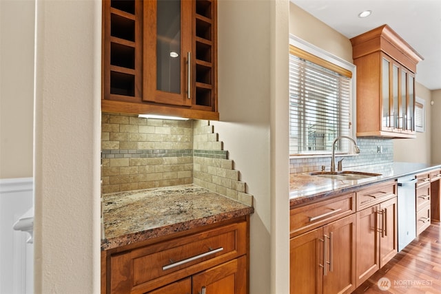 kitchen with light stone counters, glass insert cabinets, brown cabinetry, a sink, and light wood-type flooring