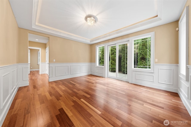 unfurnished room featuring light wood finished floors, wainscoting, and a raised ceiling