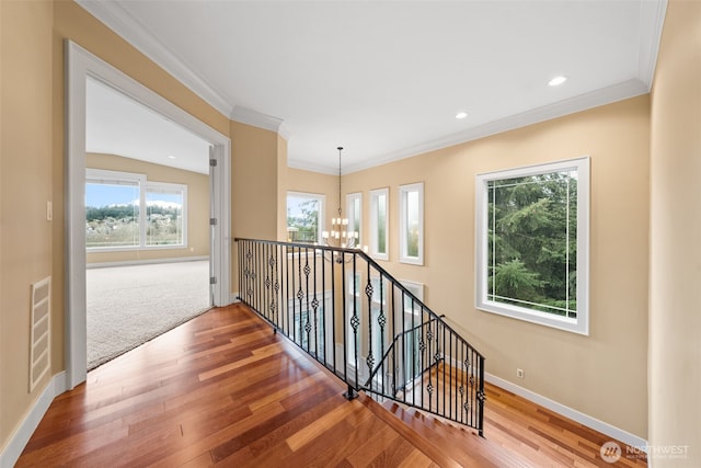 hallway with visible vents, an inviting chandelier, ornamental molding, wood finished floors, and baseboards