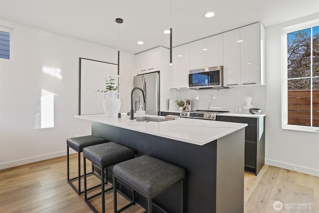 kitchen with appliances with stainless steel finishes, white cabinetry, hanging light fixtures, tasteful backsplash, and a center island with sink