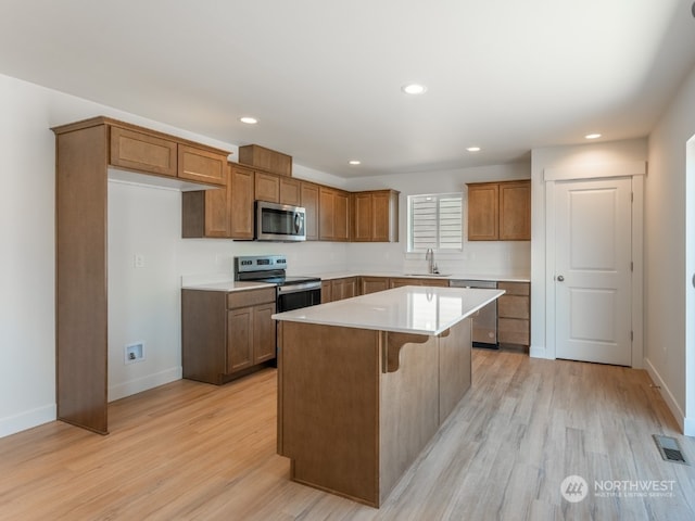 kitchen featuring sink, a kitchen breakfast bar, a center island, stainless steel appliances, and light wood-type flooring