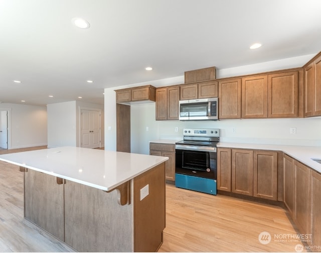 kitchen with stainless steel appliances, a kitchen island, a breakfast bar area, and light hardwood / wood-style flooring