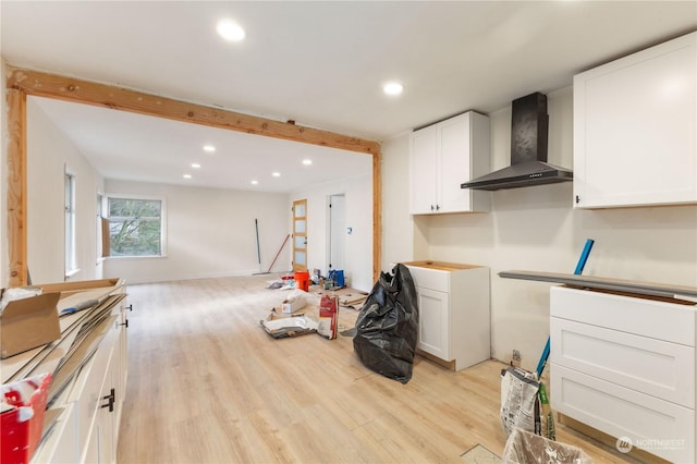 kitchen with white cabinetry, light hardwood / wood-style flooring, beamed ceiling, and wall chimney exhaust hood