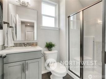 bathroom featuring a shower with door, vanity, and toilet