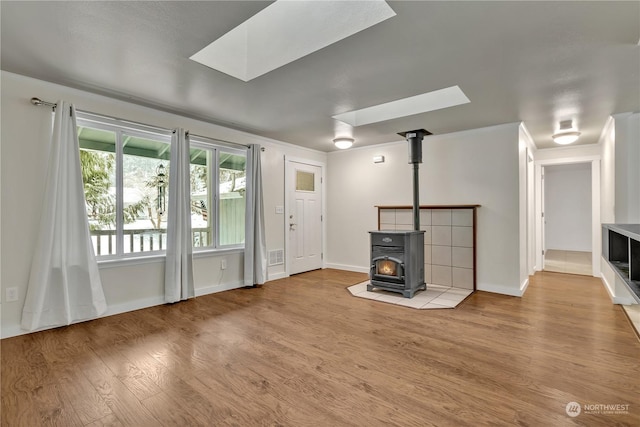 unfurnished living room featuring a skylight, a wood stove, and light hardwood / wood-style flooring