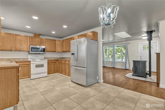 kitchen with light tile patterned flooring, appliances with stainless steel finishes, pendant lighting, a skylight, and a wood stove