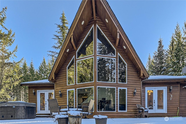 snow covered back of property with a hot tub and french doors