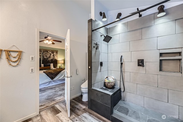 bathroom with a tile shower, ceiling fan, wood-type flooring, and toilet