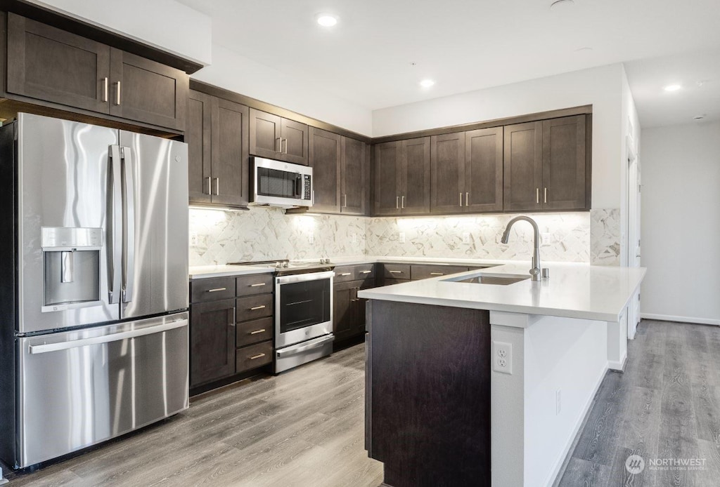 kitchen with dark brown cabinetry, appliances with stainless steel finishes, sink, and light wood-type flooring