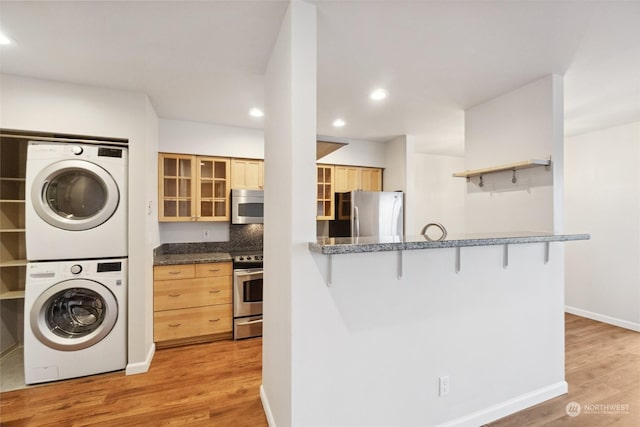 kitchen featuring light brown cabinetry, light hardwood / wood-style floors, stacked washer and clothes dryer, and appliances with stainless steel finishes