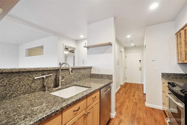 kitchen with appliances with stainless steel finishes, sink, dark stone counters, ceiling fan, and light hardwood / wood-style floors