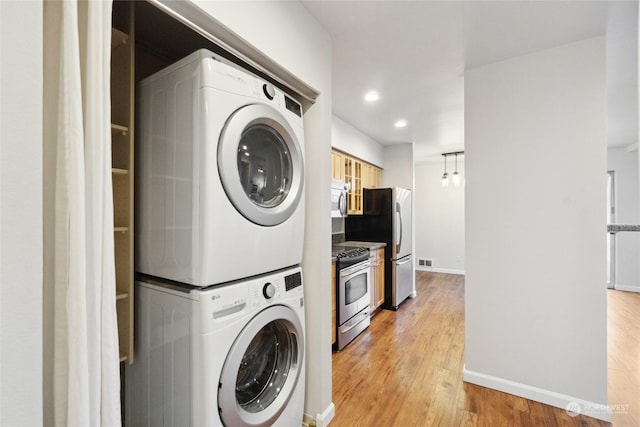 clothes washing area featuring light wood-type flooring and stacked washing maching and dryer