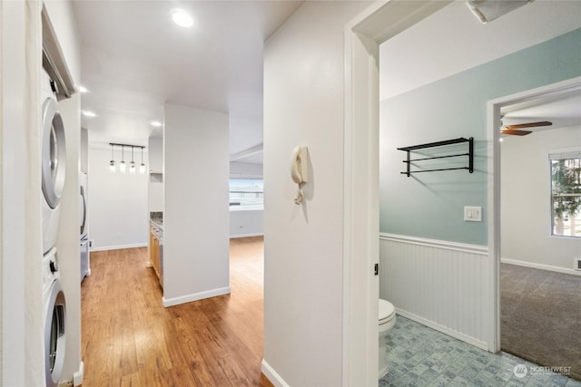 bathroom with ceiling fan, stacked washer / dryer, toilet, and hardwood / wood-style floors