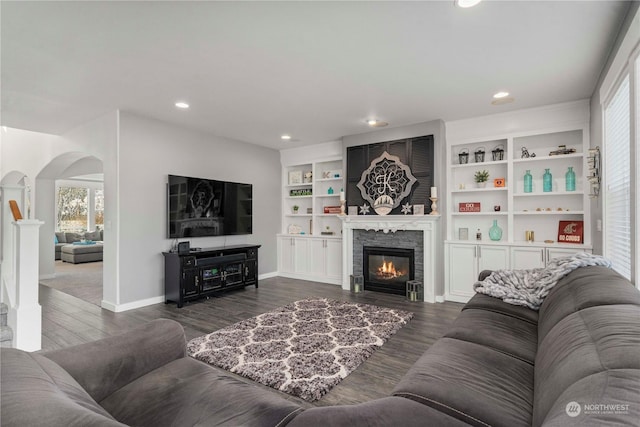 living room featuring dark wood-type flooring, a fireplace, and built in shelves