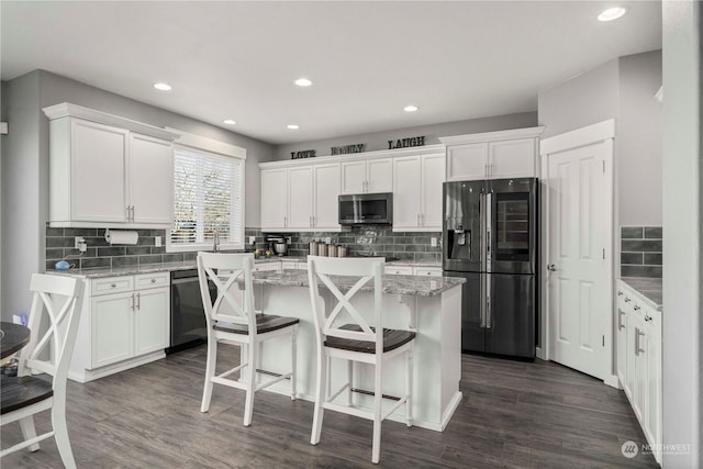 kitchen with a breakfast bar, light stone counters, a kitchen island, stainless steel appliances, and white cabinets