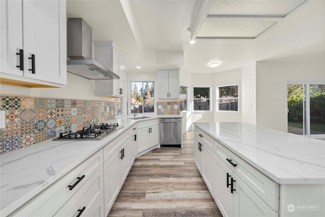 kitchen with white cabinetry, appliances with stainless steel finishes, wall chimney exhaust hood, and light stone counters