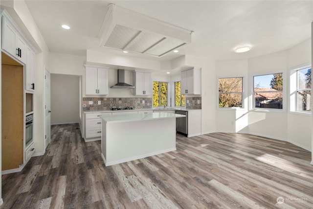 kitchen with white cabinetry, backsplash, a center island, and wall chimney range hood