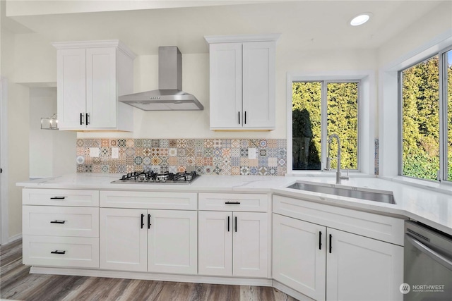 kitchen with white cabinetry, sink, stainless steel appliances, light stone countertops, and wall chimney range hood