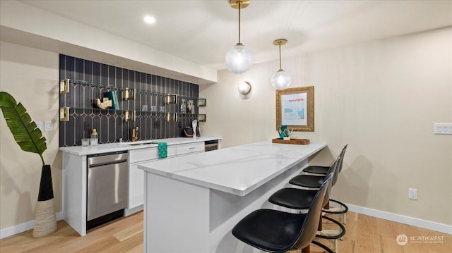 bar with pendant lighting, white cabinetry, dishwasher, light stone countertops, and light hardwood / wood-style flooring