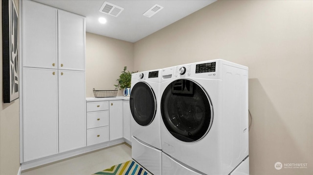 clothes washing area featuring separate washer and dryer and cabinets