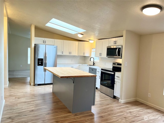 kitchen featuring vaulted ceiling with skylight, wood counters, white cabinets, a center island, and stainless steel appliances