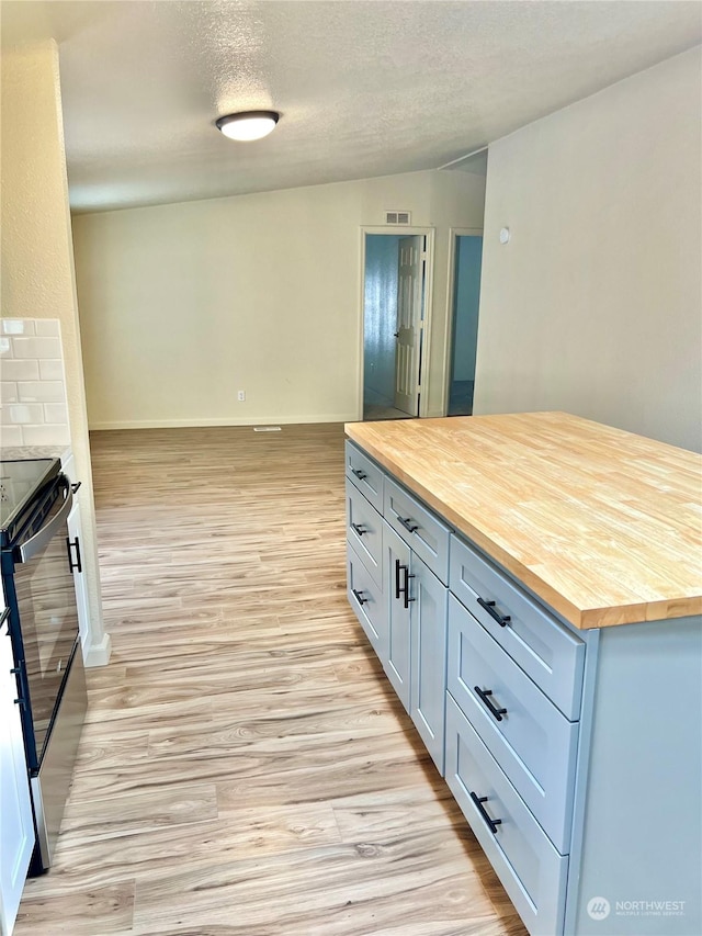 kitchen featuring butcher block counters, stainless steel range with electric cooktop, a textured ceiling, and light hardwood / wood-style flooring