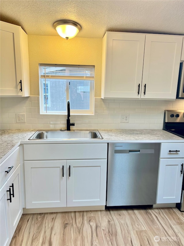 kitchen with appliances with stainless steel finishes, sink, white cabinets, decorative backsplash, and light hardwood / wood-style floors