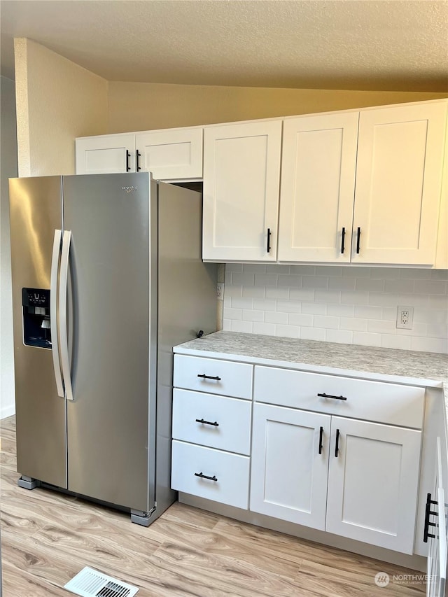 kitchen with stainless steel refrigerator with ice dispenser, white cabinetry, lofted ceiling, and light hardwood / wood-style flooring