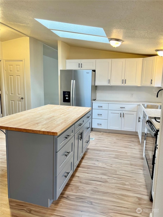 kitchen with sink, electric range oven, stainless steel refrigerator with ice dispenser, white cabinets, and wood counters