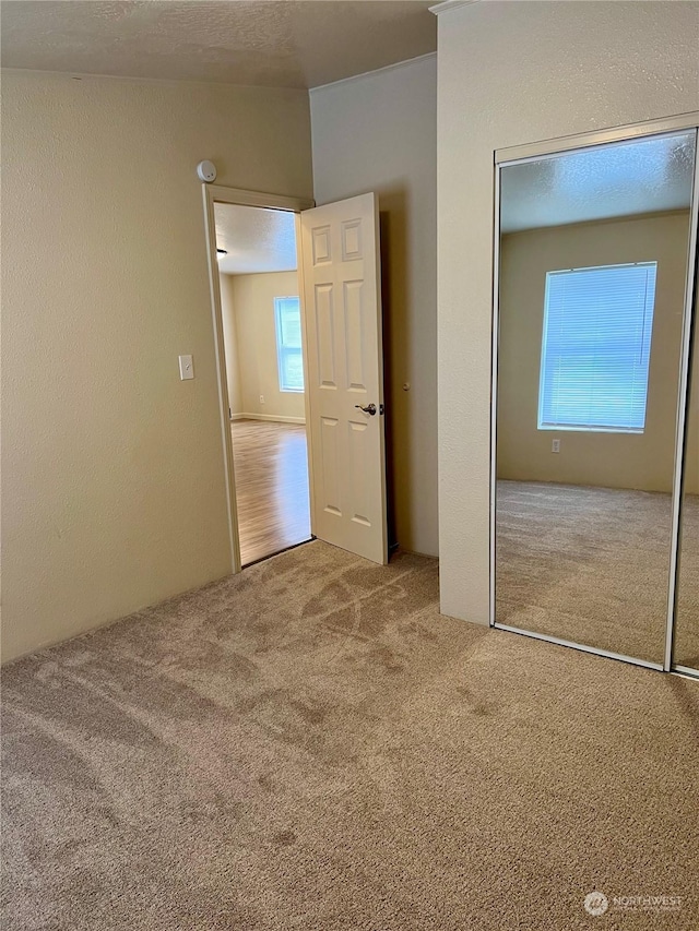 unfurnished bedroom with light carpet, a closet, and a textured ceiling