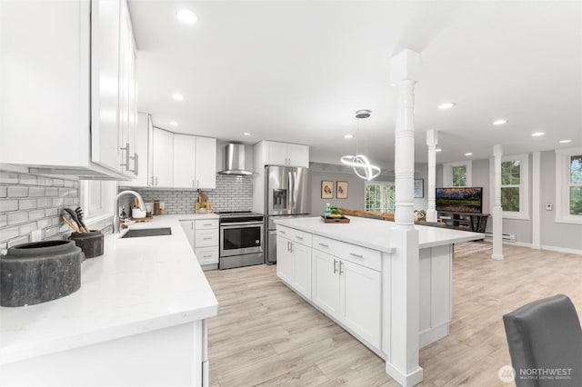 kitchen with a sink, a healthy amount of sunlight, appliances with stainless steel finishes, wall chimney exhaust hood, and decorative columns