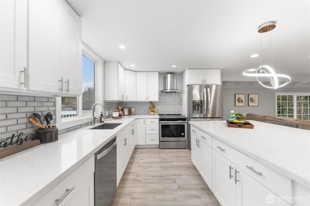 kitchen with stainless steel appliances, a sink, white cabinets, wall chimney range hood, and tasteful backsplash