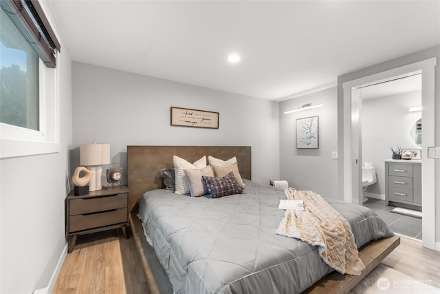 bedroom with ensuite bath, light wood-style flooring, and baseboards