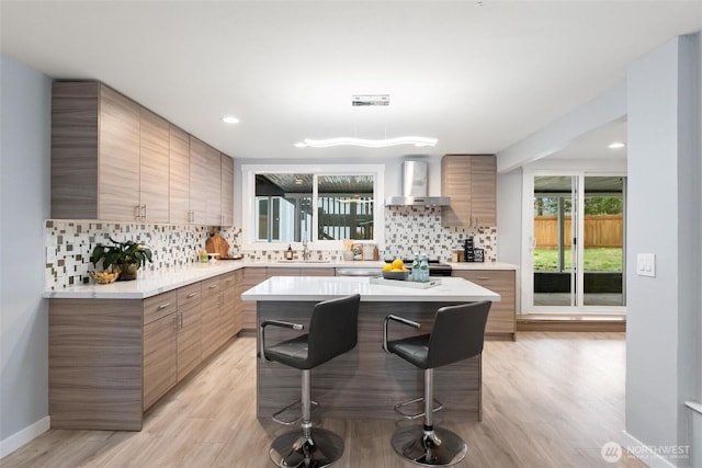 kitchen featuring decorative backsplash, modern cabinets, a breakfast bar, wall chimney range hood, and a sink