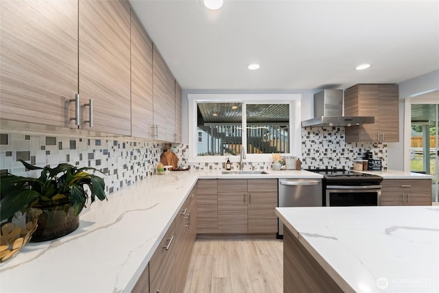 kitchen featuring appliances with stainless steel finishes, a sink, wall chimney exhaust hood, and modern cabinets