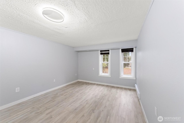 unfurnished room with a baseboard radiator, light wood-style flooring, baseboards, and a textured ceiling